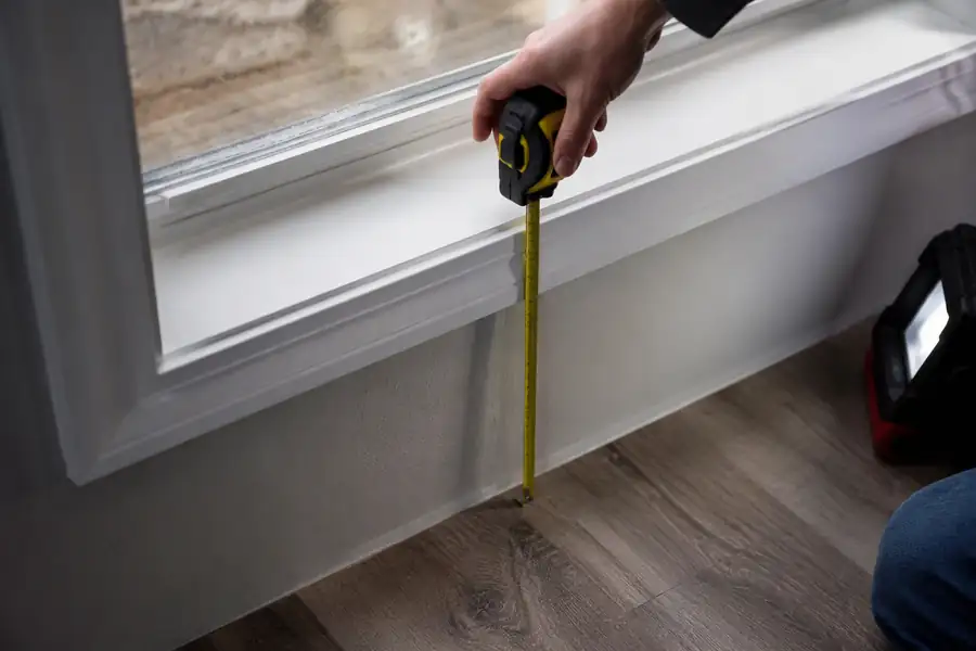 Tape measure checking the sill height of a basement egress window against the finished floor